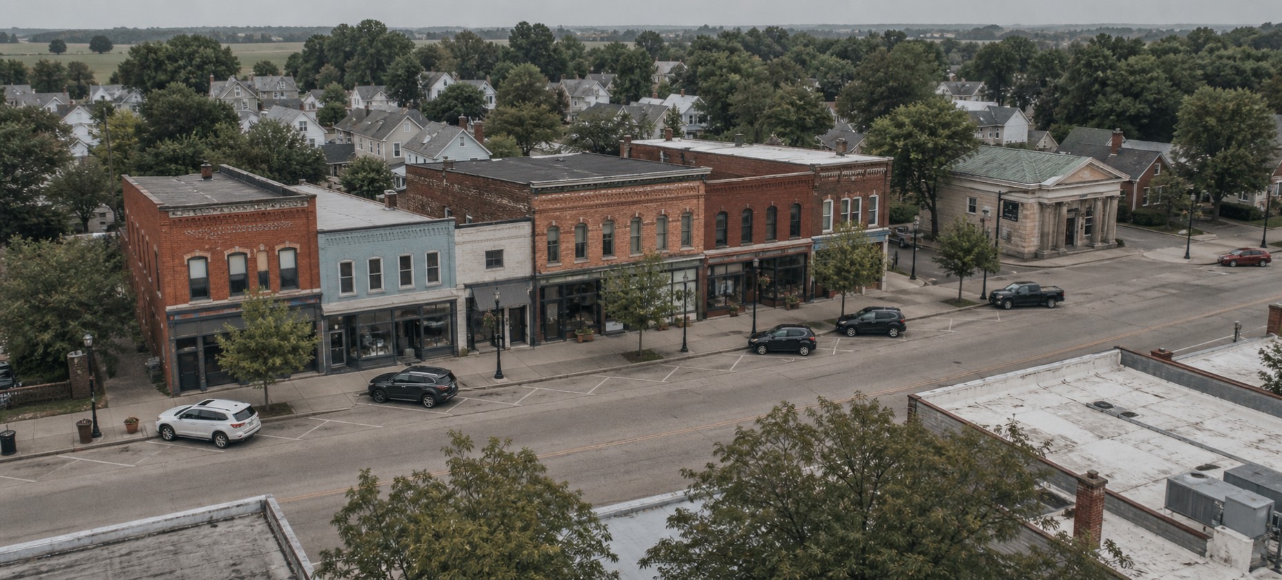 A block of brick storefronts on a small-town main street, with a stone bank building on the corner